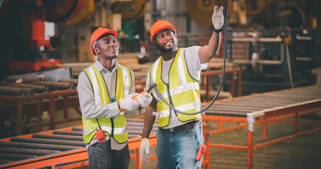 Two industrial workers wearing safety uniforms and helmets in a factory, supplied by leading uniforms suppliers in Dubai.