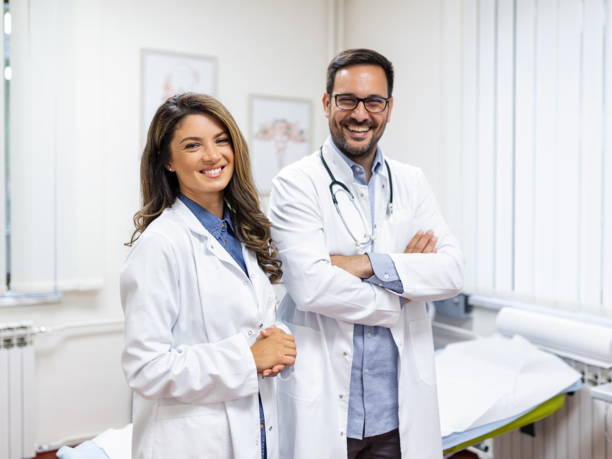 Two smiling healthcare professionals standing confidently in a medical office, showcasing uniforms provided by a leading uniforms supplier in Dubai.